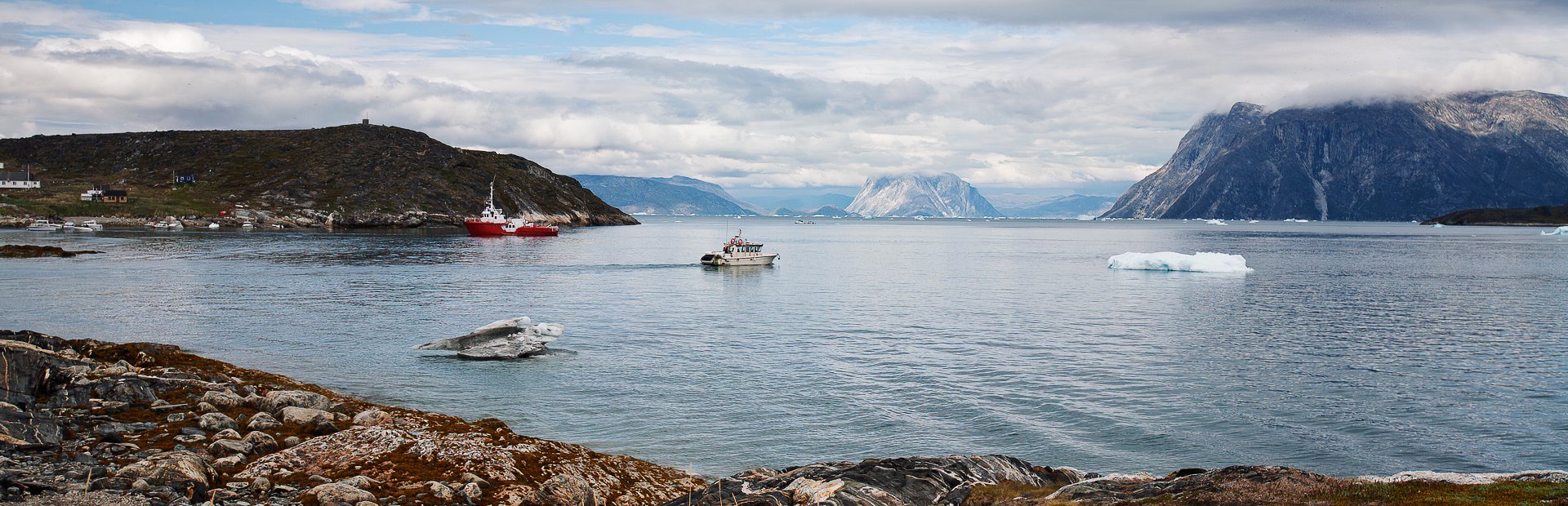 Panoramaudsigt over grønlandsk fjord med isbjerge, fiskerbåde og bjerge